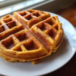 Close-up of delicious golden pumpkin waffles on a white plate, ready to be served.