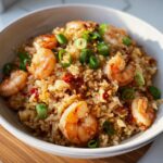 A close-up of a bowl of shrimp fried rice topped with plump shrimp and fresh green scallions.