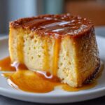 A close-up of a slice of silky flan, generously drizzled with golden caramel sauce.