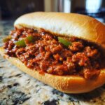 A close-up of a hearty Sloppy Joe sandwich filled with seasoned ground beef and green peppers on a soft bun.