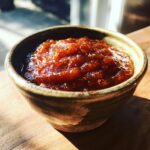 A close-up of rich, thick slow cooker apple butter in a rustic bowl, glistening in the sunlight.