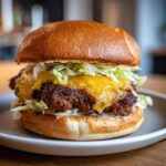A close-up of a juicy smash burger with melted cheddar cheese and shredded lettuce on a toasted bun.