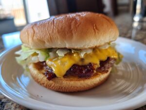 A close-up of a juicy smash burger with melted cheddar cheese, shredded lettuce, and a soft bun on a white plate.
