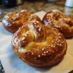 Close-up of a freshly baked soft pretzel, golden brown and sprinkled with coarse salt.