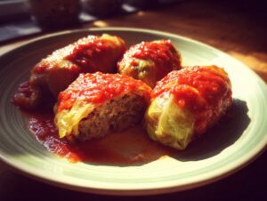 Four delicious stuffed cabbage rolls covered in tomato sauce, with one cut open to reveal the meat filling.