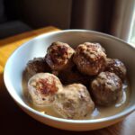 A close-up of a bowl filled with juicy Swedish meatballs coated in a rich, creamy sauce.
