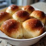 Close-up of freshly baked Texas Roadhouse rolls glistening with honey butter in a white baking dish.