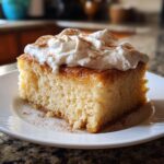 A delicious slice of Tres leches cake topped with whipped cream and a sprinkle of cinnamon.