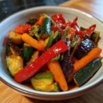 A close-up of a colorful vegetable stir fry featuring zucchini, carrots, red bell peppers, and eggplant in a glossy sauce.