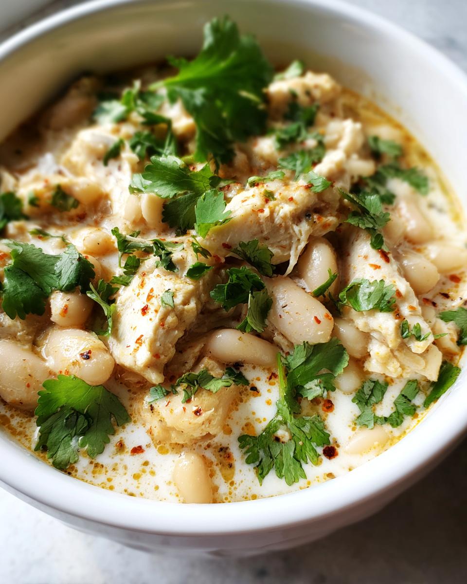 A close-up of a bowl of white chicken chili, featuring shredded chicken, white beans, and fresh cilantro.