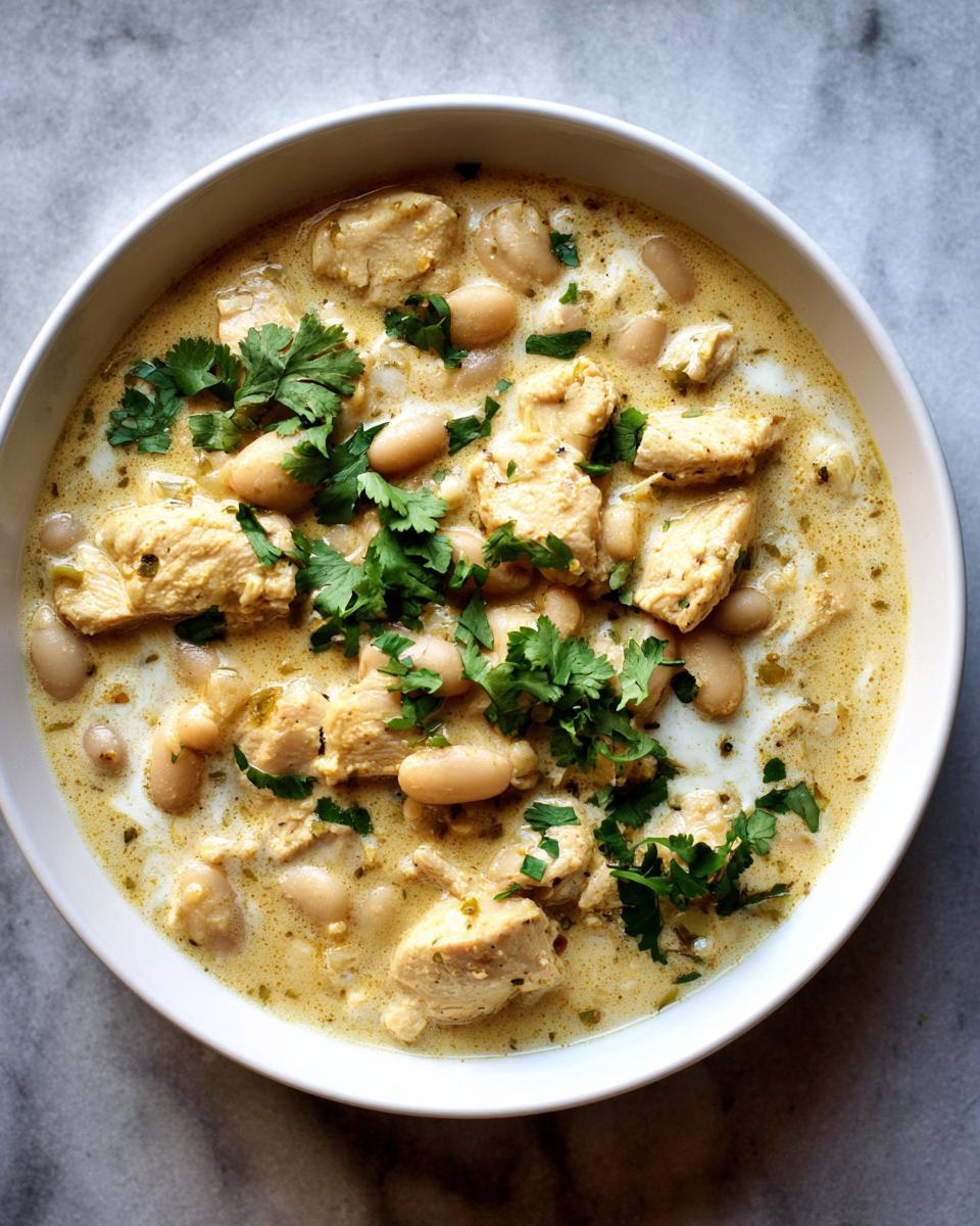 A close-up overhead view of a white bowl filled with hearty white chicken chili, garnished with fresh cilantro.