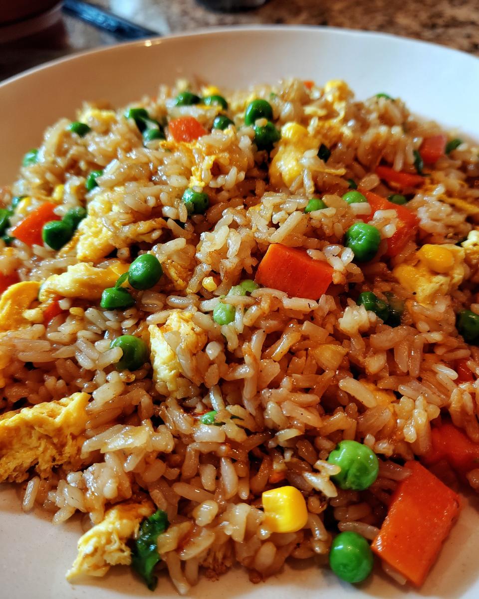 A close-up of a bowl of delicious fried rice, featuring fluffy rice, scrambled eggs, peas, carrots, and corn.