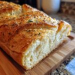 Close-up of a slice of amazing garlic bread, showing its golden-brown crust and soft, airy interior, sprinkled with herbs.