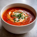 A close-up of a comforting bowl of Amazing Tomato Soup topped with a swirl of cream and fresh parsley.