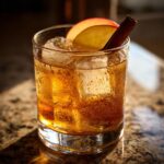 A close-up of a chilled Apple Cider Cocktail in a glass, garnished with an apple slice and cinnamon stick.