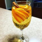 A bubbly Apple Cider Spritz Cocktail garnished with orange slices, orange peel, and a cinnamon stick in a champagne flute.