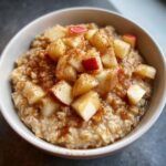 A close-up of a bowl of Apple Cinnamon Oatmeal topped with diced apples and a drizzle of syrup.