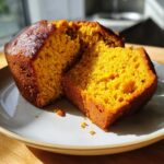 A close-up of a slice of moist Autumn Harvest Pumpkin Bread on a plate, showing its vibrant orange interior.