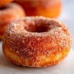 Close-up of a freshly baked apple cider donut coated in cinnamon sugar.