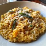 A close-up view of a creamy Baked Butternut Squash Risotto, garnished with fresh sage leaves and grated Parmesan cheese.
