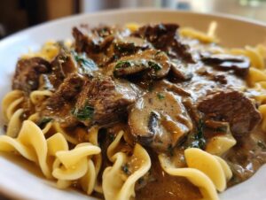 A close-up of rich Beef Stroganoff served over wide egg noodles, with mushrooms and parsley.