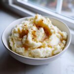 A close-up of creamy brown butter mashed potatoes in a white bowl, drizzled with rich brown butter.