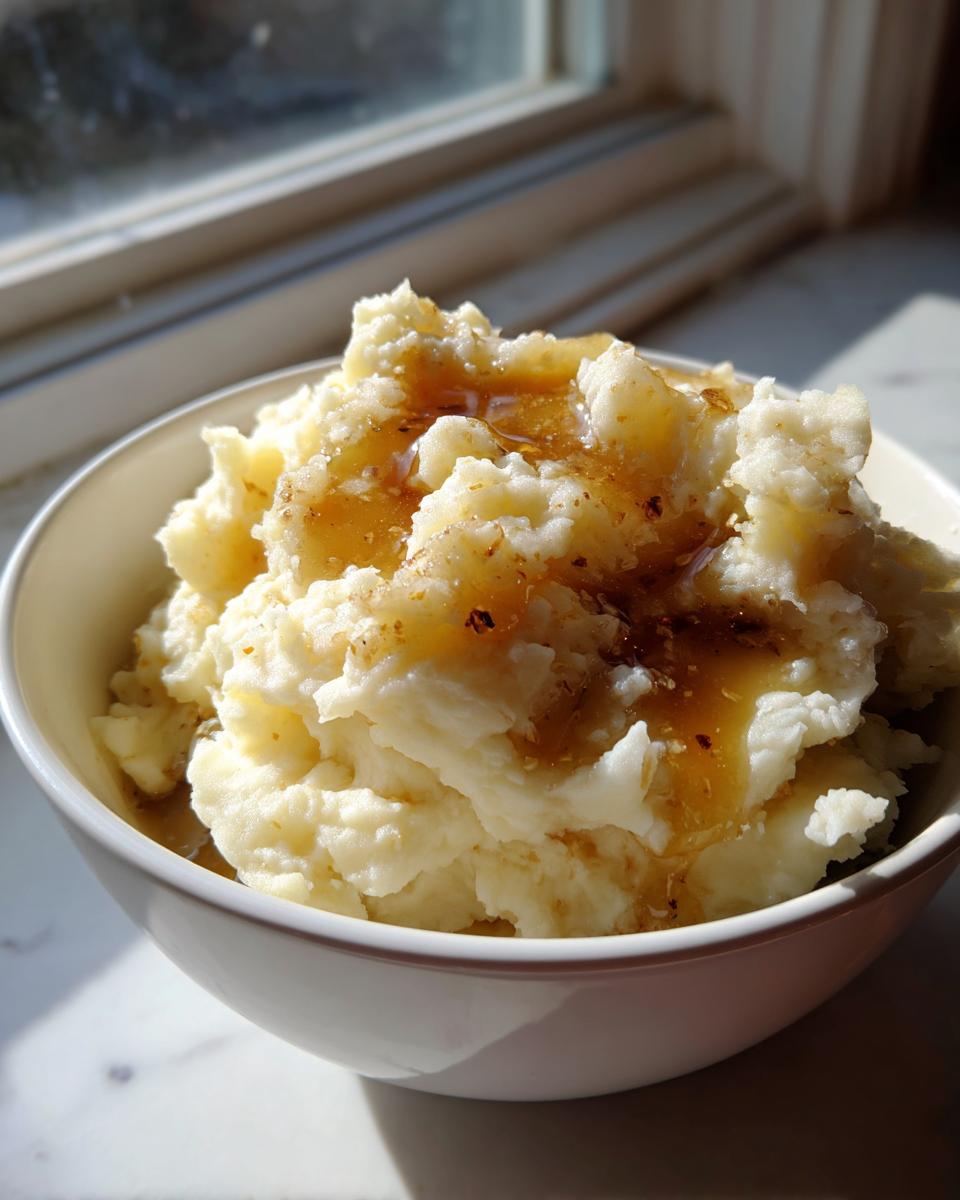 A close-up of creamy brown butter mashed potatoes drizzled with sauce in a white bowl.
