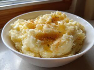 A close-up of fluffy brown butter mashed potatoes in a white bowl, drizzled with melted butter and sprinkled with herbs.