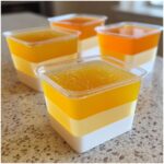 Close-up of layered Candy Corn Jello Shots in clear plastic cups, showing white, yellow, and orange layers.