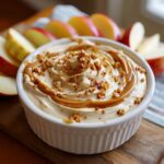 A creamy Caramel Apple Dip swirled with caramel sauce and topped with chopped nuts, served with apple slices.