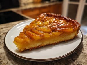 A close-up of a slice of Caramel Apple Tarte Tatin on a white plate, showcasing the glossy caramel and tender apple slices.