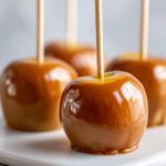 Close-up of four glossy caramel apples on wooden sticks, ready to be enjoyed.