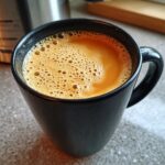 A close-up of a steaming black mug filled with a frothy, golden-brown chai latte.