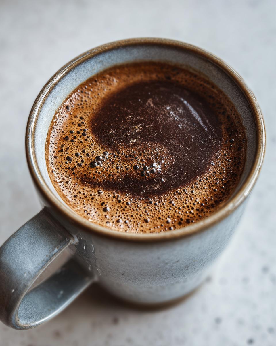 A close-up shot of a mug filled with frothy, dark brown Champurrado, showcasing its rich texture and bubbly surface.