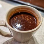 A close-up of a steaming mug of rich, dark Champurrado, sprinkled with cinnamon.