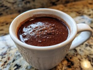 Close-up of a steaming mug of rich, dark Champurrado, dusted with cocoa powder.