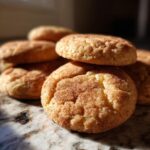 A close-up of a stack of chewy snickerdoodles, coated in cinnamon sugar, on a marble countertop.
