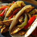 Close-up of three chicken fajitas filled with seasoned chicken strips, red and green bell peppers, and onions.