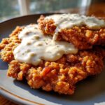 Close-up of two golden-brown, crispy chicken fried steaks smothered in creamy white gravy.