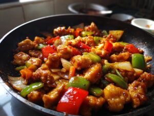Close-up of a sizzling chicken stir fry with colorful bell peppers and onions in a black pan.