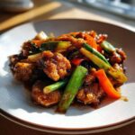 A close-up of a plate of delicious chicken stir fry, featuring tender chicken pieces, crisp green onions, and vibrant red bell peppers in a savory sauce.
