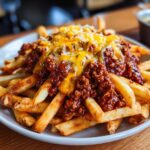 A close-up of golden crispy french fries generously topped with savory chili and melted cheese.