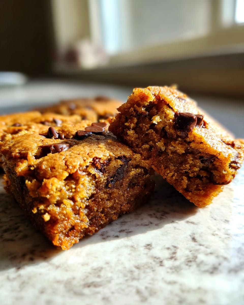 Close-up of two rich, chewy chocolate chip blondies, one broken in half to reveal the gooey interior.