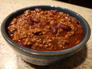A close-up view of a blue bowl filled with hearty classic beef chili, featuring ground beef and kidney beans.