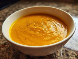 A close-up of a white bowl filled with creamy Classic Butternut Squash Soup, garnished with black pepper.