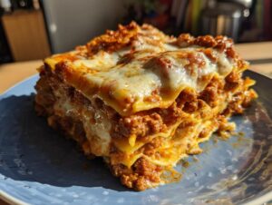 A generous slice of classic lasagna with layers of pasta, rich meat sauce, and melted cheese, served on a blue plate.