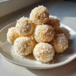 A pile of freshly made Coconut Ladoo balls, coated in shredded coconut, served on a light gray plate.