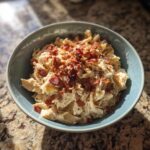 A close-up of a bowl filled with creamy crack chicken topped with crispy bacon bits.
