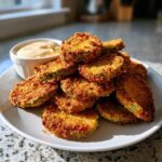 A pile of golden-brown, crispy fried pickles served with a creamy dipping sauce on a white plate.