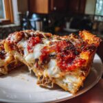 A close-up of a thick slice of deep dish pizza with melted cheese, rich tomato sauce, and a golden crust.